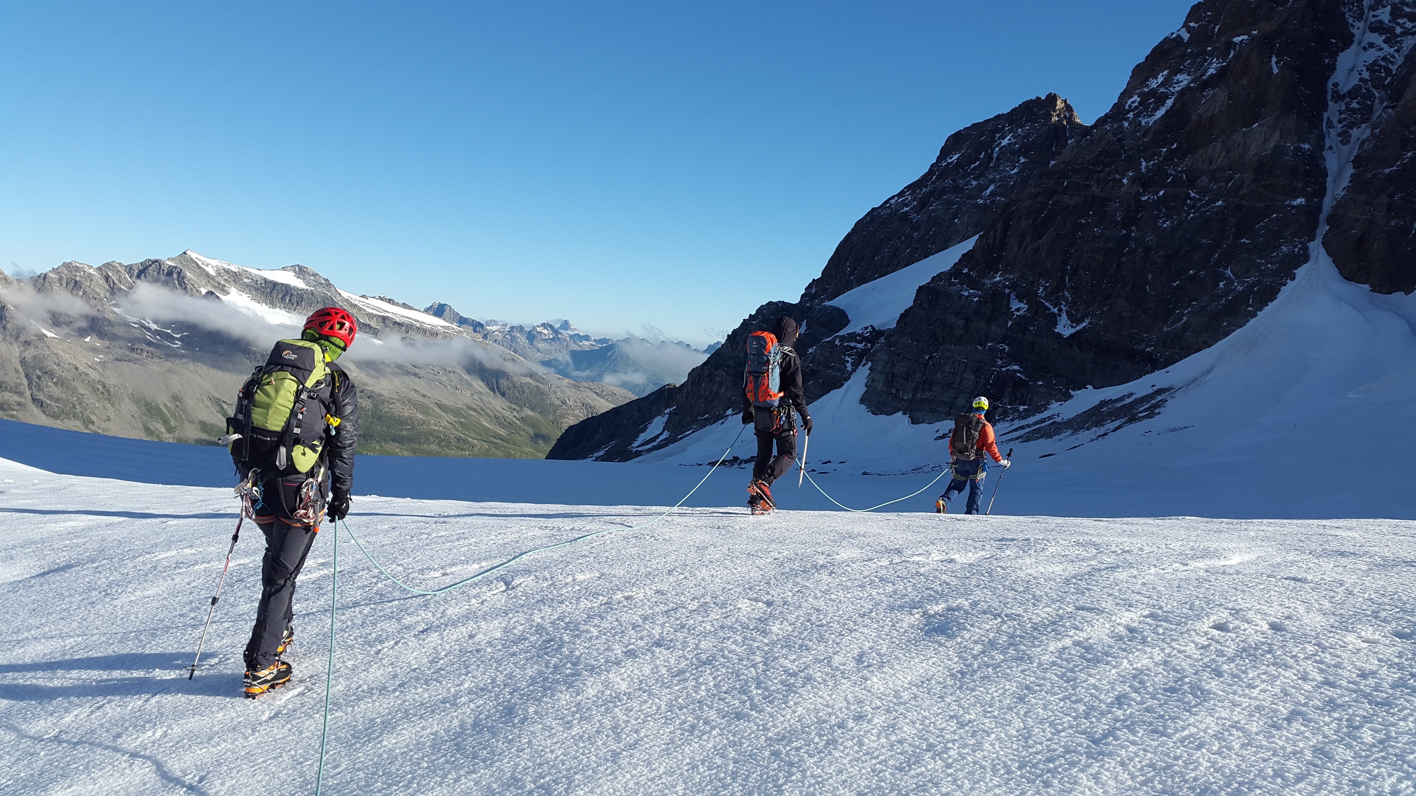 Eine Gruppe von Menschen mit Rucksäcken und Kletterausrüstung besteigt einen verschneiten Berg, passend für Outdoor-Abenteuer und Bergsport.