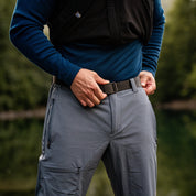 Nahaufnahme der Softshell Wanderhose Herren beim Anpassen eines schwarzen Gürtels an hellgrauer Trekkinghose; ideal für Outdoor-Abenteuer mit leichtem, elastischem Material und sportlichem Schnitt.