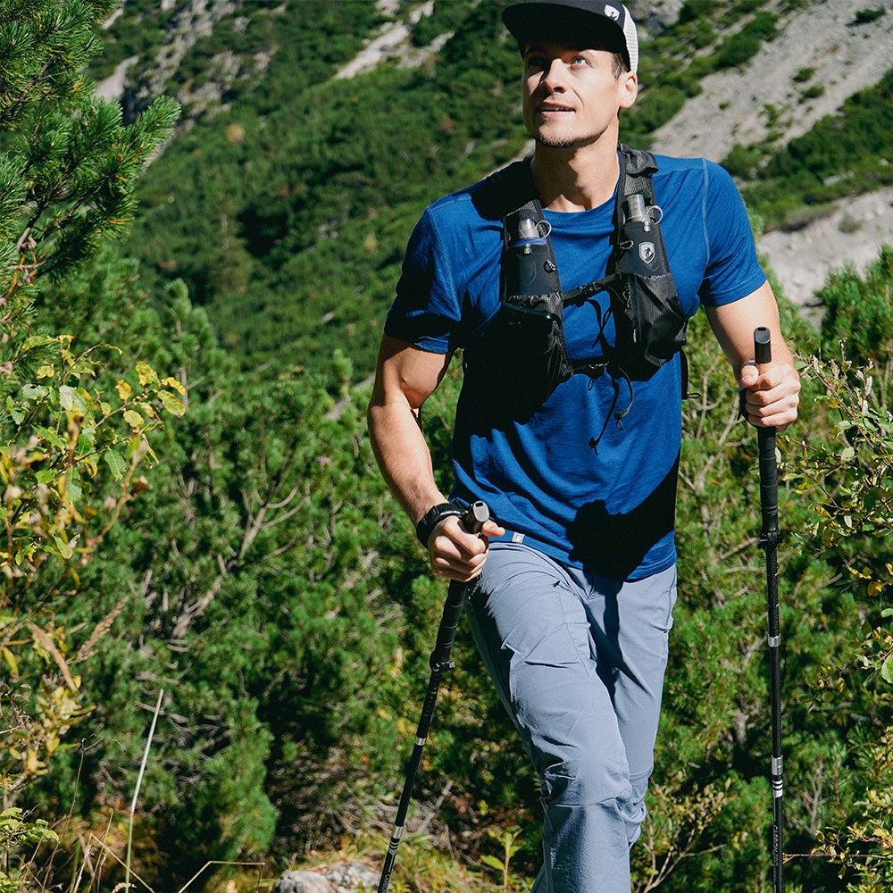 m2, Trekkingstöcken und Wasservest unterwegs auf einem bewaldeten Bergpfad. Ideal für Outdoor-Aktivitäten.