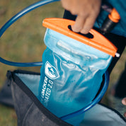 Trinkblase für Sommer + Winter: Nahaufnahme der blauen Wasserblase mit orangefarbener Verschlussklemme und Trinkschlauch, aus einem Rucksack gezogen, ideal für Outdoor-Sport.
