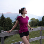 Frau lehnt am Zaun, trägt Merino Coolmax T-Shirt Damen 150 g/m2. Ideal für Outdoor-Aktivitäten, bietet Komfort und Funktion durch Merinowolle und Coolmax-Technologie.
