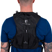 Laufweste Trail Pro 5 mit 2 Flaschen, schwarze Alpin Loacker Hydrationsweste mit Taschen, Kordelkapuze, ideal für Trailrunning, über blauem T-Shirt getragen.