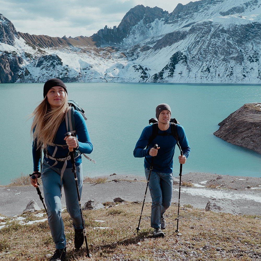 Zwei Wanderer tragen das Merino Langarm Shirt Damen 230 g/m2 von Alpin Loacker, ideal für Outdoor-Aktivitäten, vor einer alpinen Seen- und Berglandschaft.