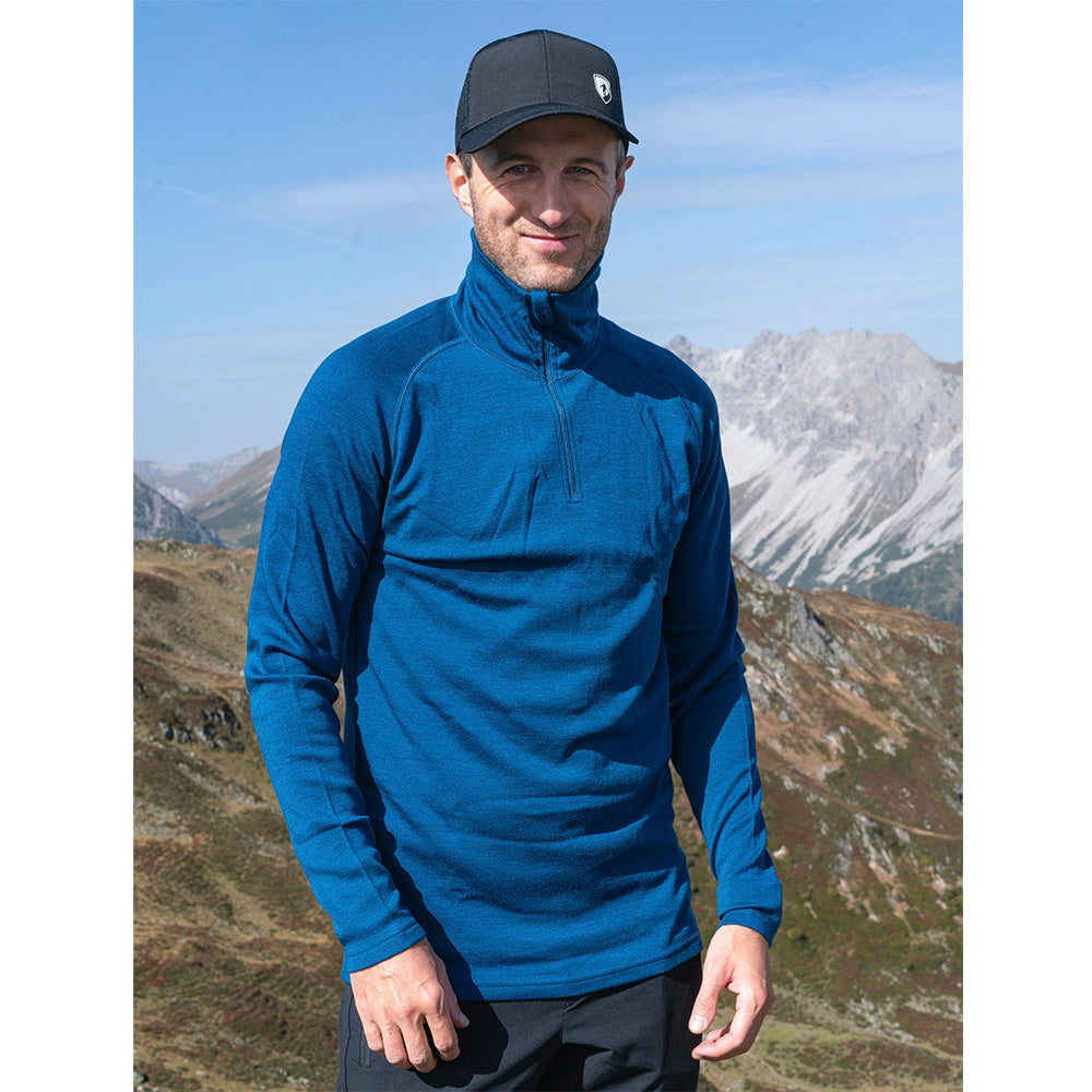 Mann in alpiner Landschaft trägt das Merino Langarmshirt mit Zip Herren 230 g/m², ideal für Outdoor-Aktivitäten, aus 100% Merinowolle für Komfort und Funktionalität.