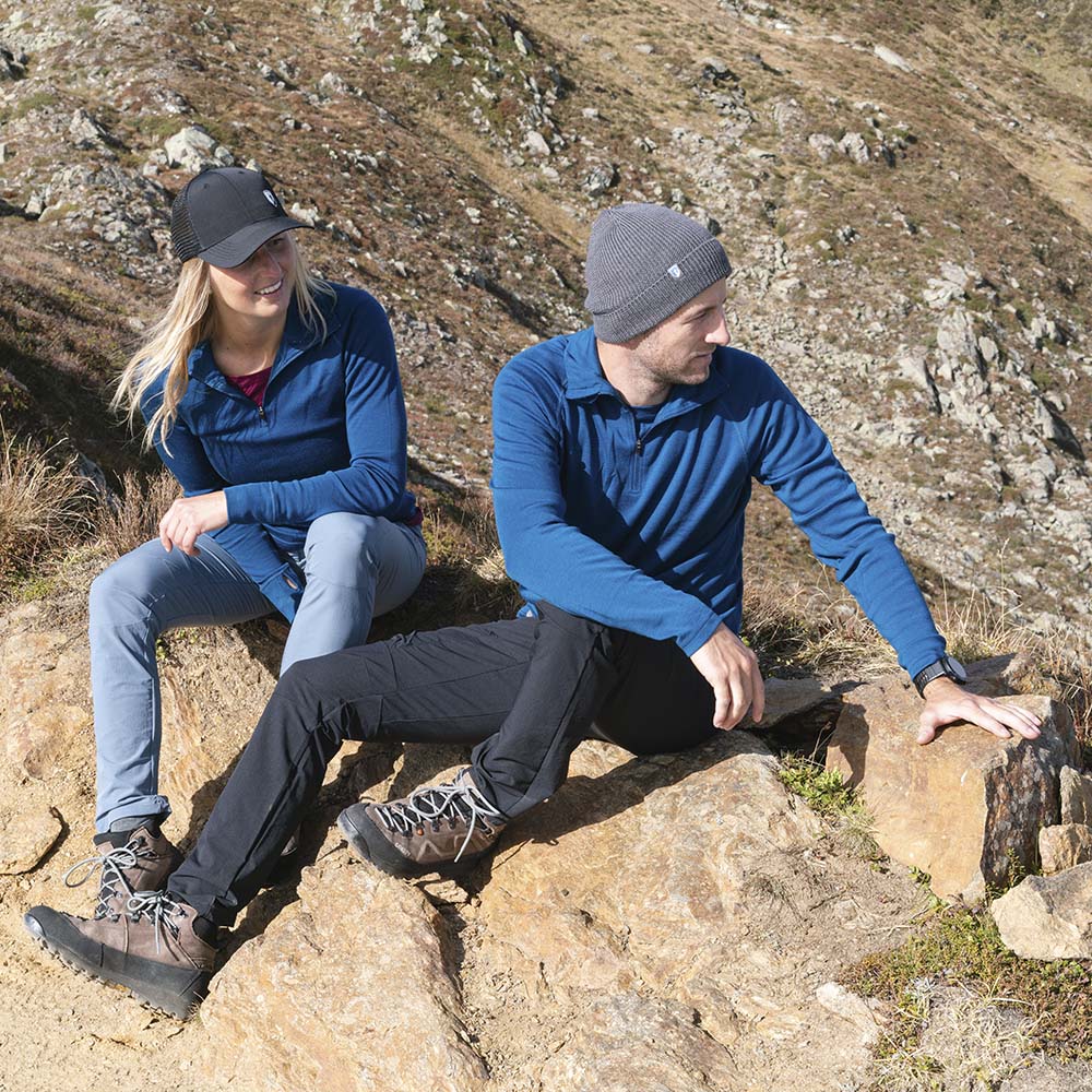 Zwei Wanderer pausieren auf einem felsigen Hang, der Mann trägt die Merino Mütze Herren & Damen Strick 230g/m² für optimalen Komfort und Temperaturregulierung.