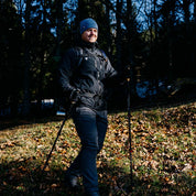 Person beim Wandern im Wald, trägt Herren 3 Lagen Hardshell Regenjacke von Alpin Loacker, ausgestattet mit Trekkingstöcken und Rucksack, ideal für Outdoor-Aktivitäten.