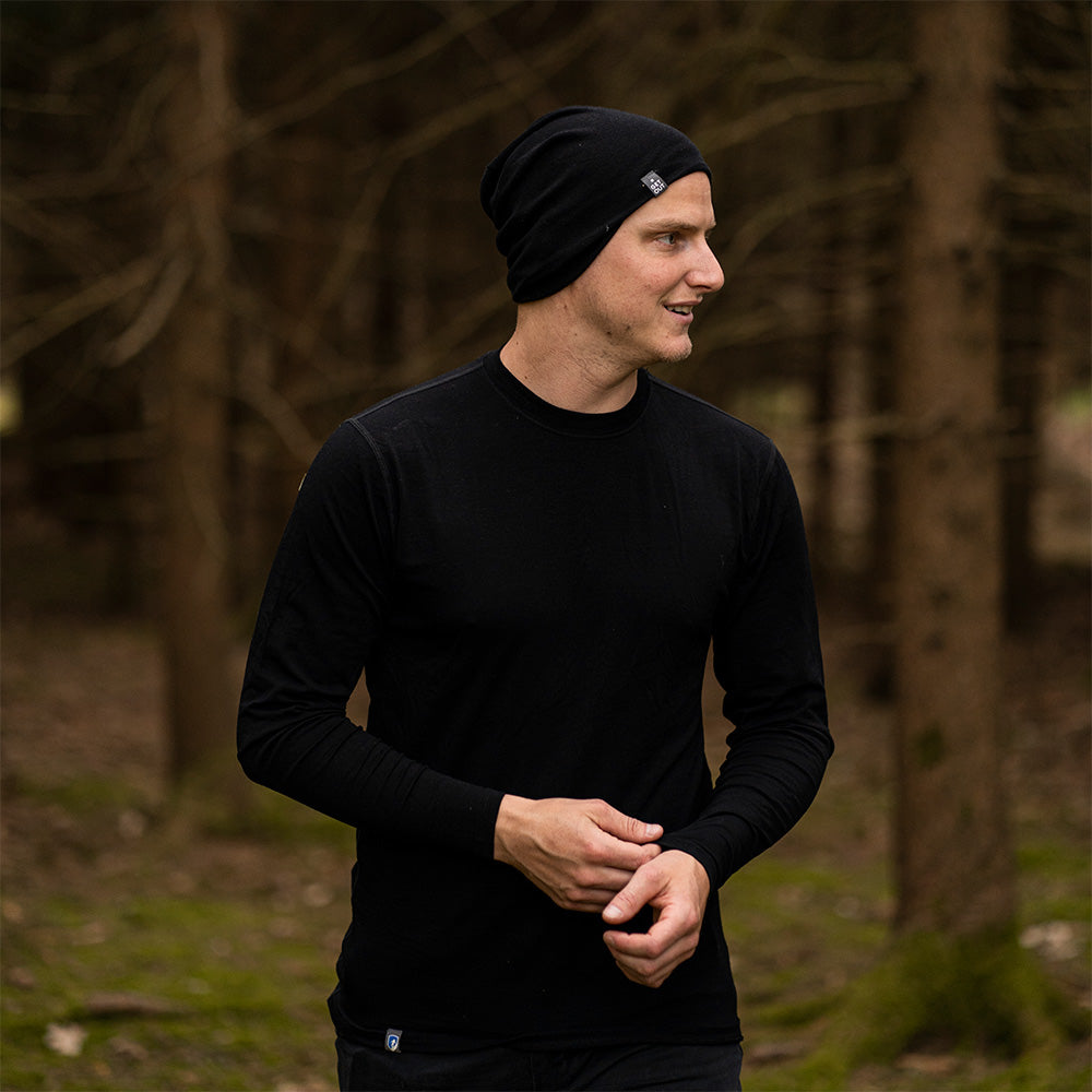 Junger Mann im Wald trägt das Merino Langarm Shirt Herren 150 g/m², ideal für Outdoor-Aktivitäten dank temperaturregulierender Merinowolle und CORESPUN-Technologie.