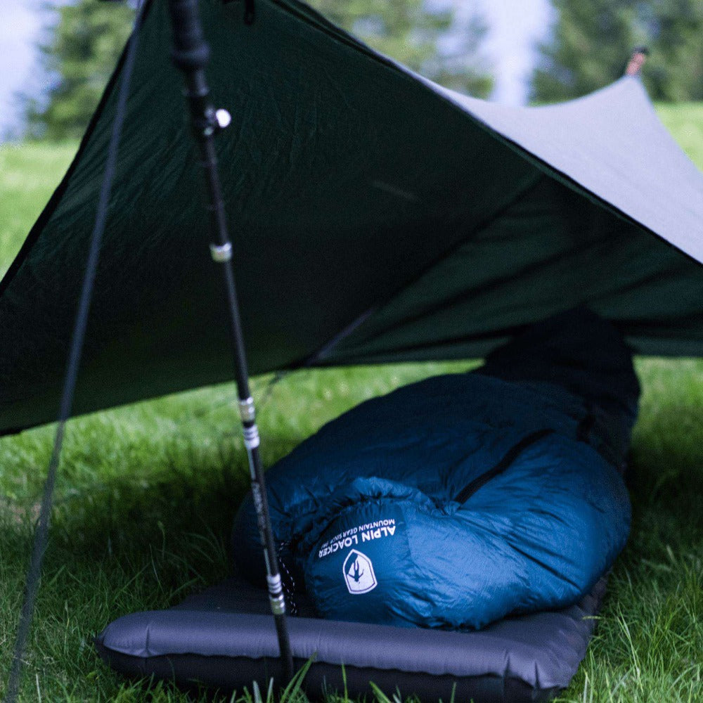 Leichter Tarp-Unterstand mit trekkingstockgestütztem Down Pro 3 Jahreszeiten Schlafsack 860g und Isomatte auf Gras für ultraleichtes Camping.