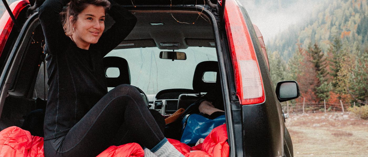 Eine Frau sitzt im Auto mit einem blauen Rucksack und rotem Tuch, möglicherweise beim Wandern oder Outdoor-Aktivität.