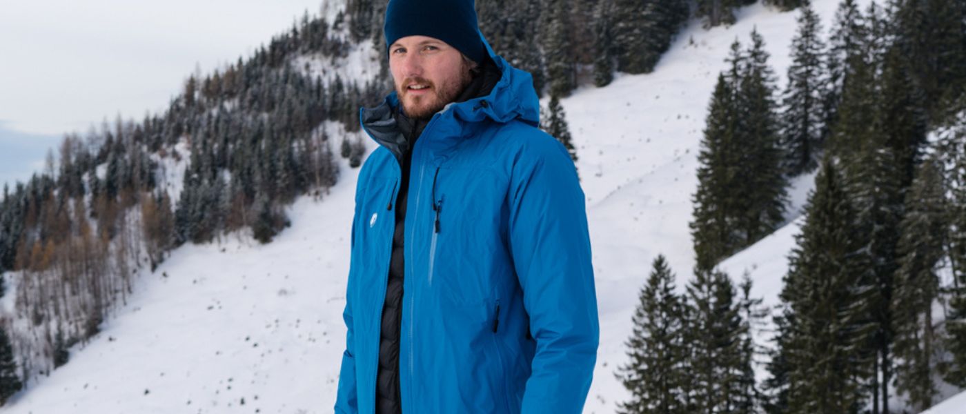 Ein Mann in einer blauen Jacke steht im Schnee, passend für Outdoor-Aktivitäten, wie sie auf alpinloacker.com angeboten werden.