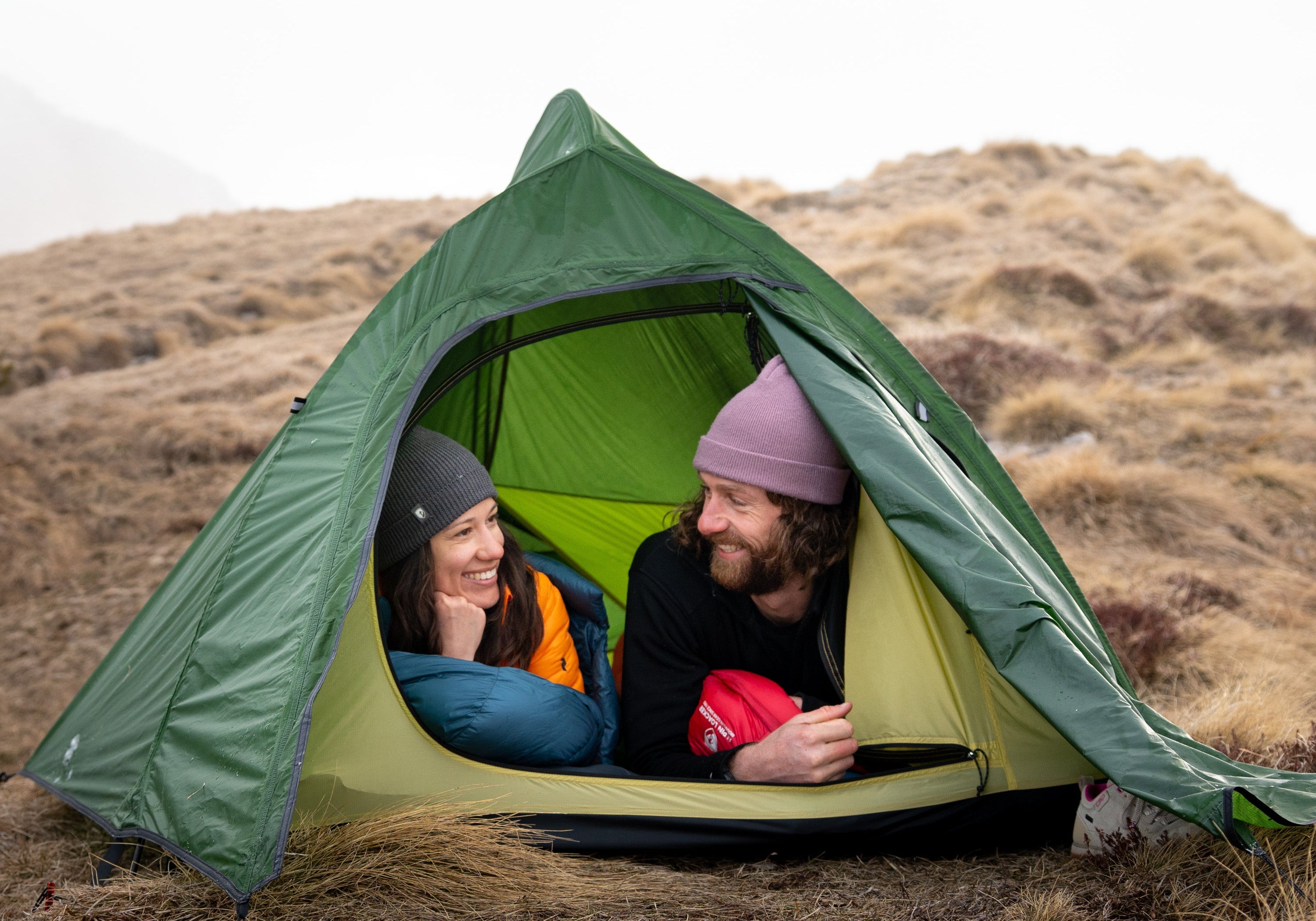 Eine Frau kniet in einem Zelt, umgeben von Pflanzen, passend zur Outdoor-Ausrüstung von Alpinloacker für Camping und Wandern.