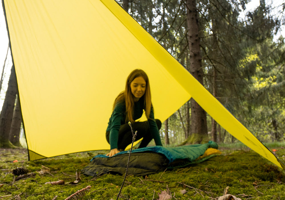 Eine Frau kniet in einem Zelt, umgeben von Pflanzen, passend zur Outdoor-Ausrüstung von Alpinloacker für Camping und Wandern.