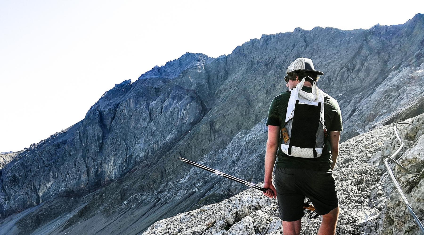 Ein Mann mit Rucksack und Wanderstock steht auf einem felsigen Berg, passend zur Outdoor-Ausrüstung von alpinloacker.com für Abenteuer in der Natur.