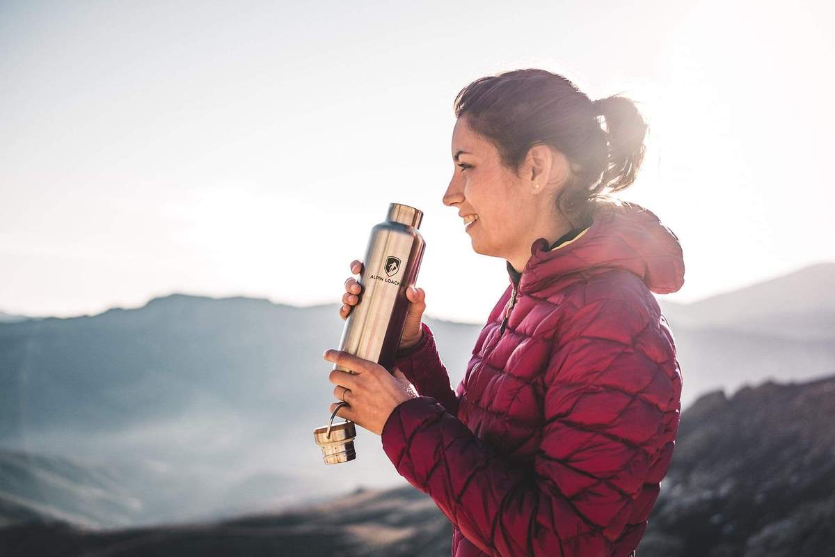 Eine Frau hält eine Wasserflasche, ideal für Outdoor-Aktivitäten wie Wandern, passend zum Sortiment von Alpinloacker für Abenteuerausrüstung.