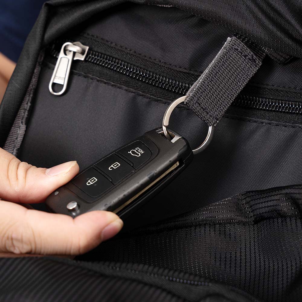 Person hält Autoschlüssel und 30-Liter Alpin Loacker Wanderrucksack, ideal für Outdoor-Abenteuer, mit ergonomischem Design und atmungsaktivem Rückensystem, im Hintergrund sichtbar.