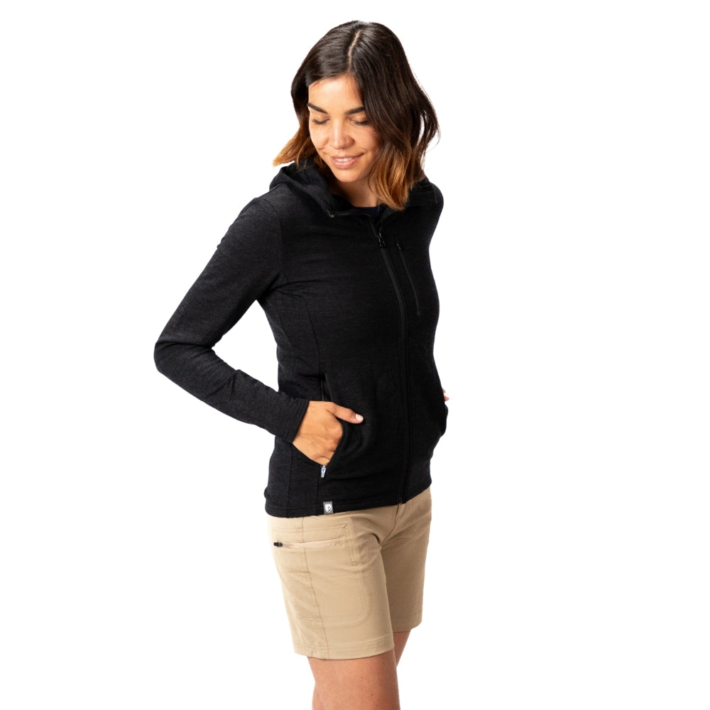 Merino Hoody Damen - 270g/m²: Modell trägt schwarzen, taillierten Hoodie aus Merinowolle, ideal für Outdoor-Aktivitäten, mit praktischen Seitentaschen und elastischem Stoff für Komfort.