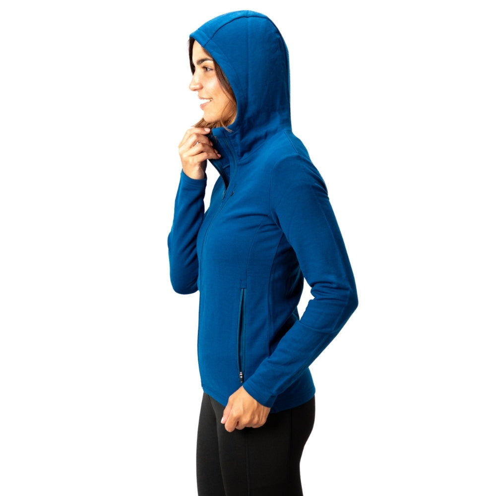 Merino Hoody Damen - 270g/m2: Frau trägt einen funktionalen, elastischen Hoody aus Merinowolle und Bambus, ideal für Outdoor-Aktivitäten, mit YKK-Reißverschlüssen und eng anliegender Kapuze.