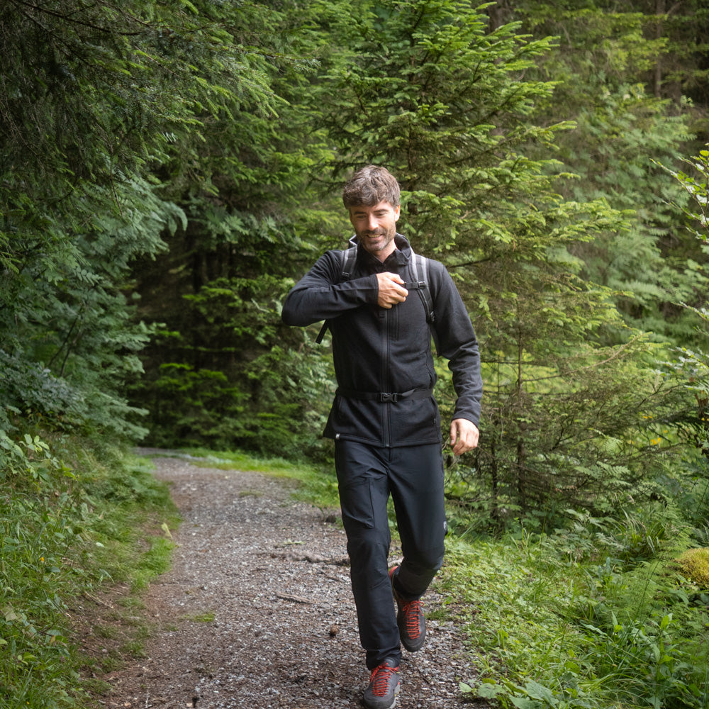 Mann läuft mit schwarzem Merino Hoody durch die Natur, das perfekte Kleidungsstück für Outdooraktivitäten