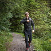 Mann läuft mit schwarzem Merino Hoody durch die Natur, das perfekte Kleidungsstück für Outdooraktivitäten