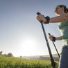 Frau benutzt Alpin Loacker Teleskop Nordic Walking Stöcke aus Aluminium auf einem Feld, zeigt ergonomische Griffe und verstellbare Länge.