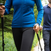 Merino Hoody Damen - 270g/m2: Zwei Personen mit Trekkingstöcken auf Waldweg; vordere Person trägt den atmungsaktiven, elastischen Hoody, ideal für Outdoor-Abenteuer.