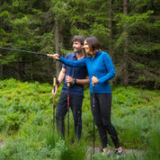 Zwei Personen wandern im Wald mit Trekkingstöcken, die Frau trägt den Merino Hoody Damen - 270g/m², ideal für Outdoor-Aktivitäten bei kühlem Wetter.