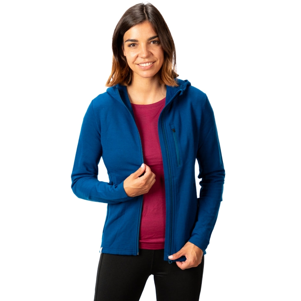 Junge Frau in Merino Hoody Damen - 270g/m², zieht Reißverschluss hoch. Ideal für Outdoor-Aktivitäten, atmungsaktiv, elastisch und weich. Perfekt für kältere Bedingungen.