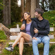 Merino Hoody Damen - 270g/m²: Paar auf Holzbank im Wald, Frau trägt funktionalen Hoody, ideal für Outdoor-Aktivitäten. Natürliche Merinowolle, atmungsaktiv und elastisch.