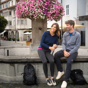 Paar in Freizeitkleidung sitzt am Brunnenrand, trägt Alpin Loacker 100% Merinowolle Jacke Herren 160 g/m² - ultrafein, ideal für Outdoor-Aktivitäten.