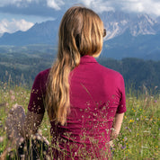 Dame sitzt in berry farbenem Merino Coolmax Polo am Berg in einer Wiese