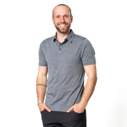 Model posiert in grauem Merino Coolmax Polo mit Händen in den Taschen vor weißem Hintergrund