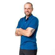 Model posiert mit verschränkten Armen vor weißem Hintergrund im blauen Merino Coolmax Polo von Alpin Loacker