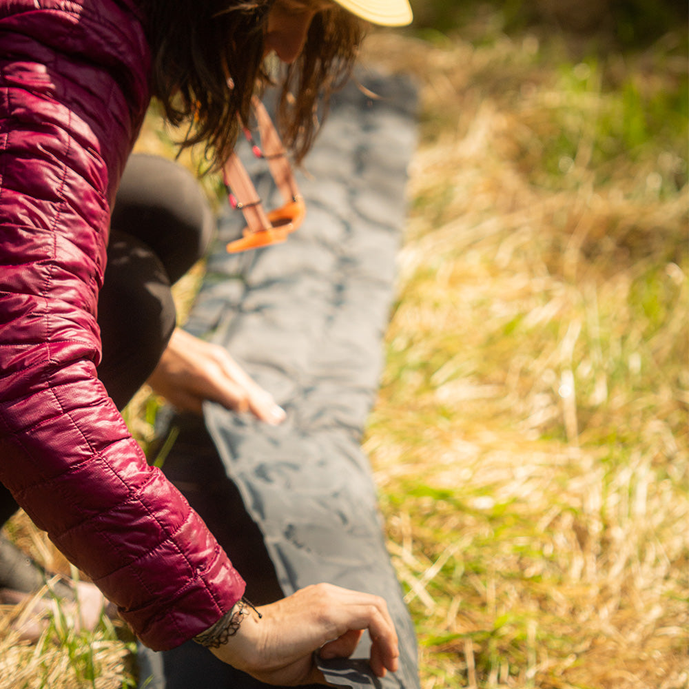 Frau faltet Zelt neben ultraleichter Isomatte Air Light, ideal für Camping, aus recyceltem Material, leicht und kompakt für Outdoor-Abenteuer.