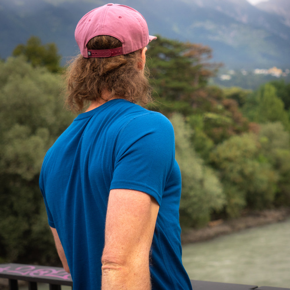 Mann steht mit blauem Merino Coolmax T-Shirt auf einer Brücke