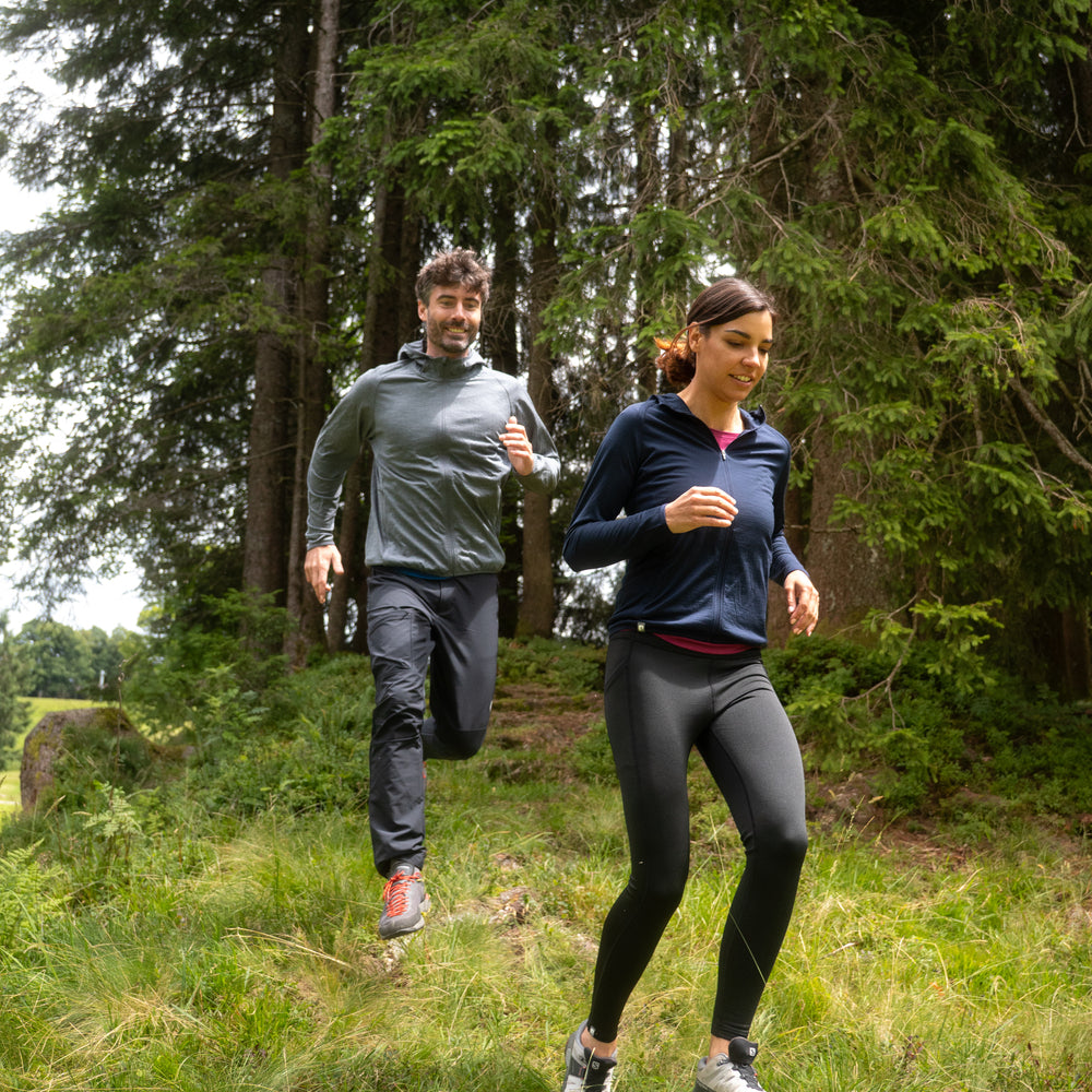Zwei Personen joggen auf einem Waldpfad, beide tragen die 100% Merinowolle Jacke Damen 160 g/m² - ultrafein, ideal für Outdoor-Abenteuer.