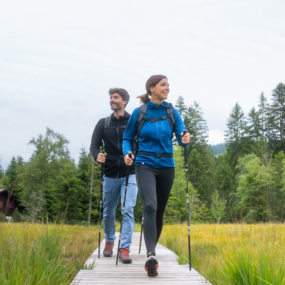 Zwei Wanderer auf Holzsteg im Wald tragen den 100% Merino Sport Hoody mit Zip Damen - 230g/m2, ideal für Outdoor-Aktivitäten, mit praktischer Brusttasche.