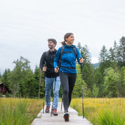 Zwei Wanderer auf Holzsteg im Wald tragen den 100% Merino Sport Hoody mit Zip Damen - 230g/m2, ideal für Outdoor-Aktivitäten, mit praktischer Brusttasche.