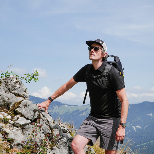 Homme grimpant sur des rochers, porte le polo mérino homme 150 g/m² - NOUVEAU, idéal pour les activités de plein air avec respirabilité et régulation de la température.