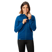 Frau zipt einen blauen 100% Merino Sport Hoody mit Zip Damen - 230g/m², ideal für Outdoor-Aktivitäten, kombiniert mit schwarzen Leggings.