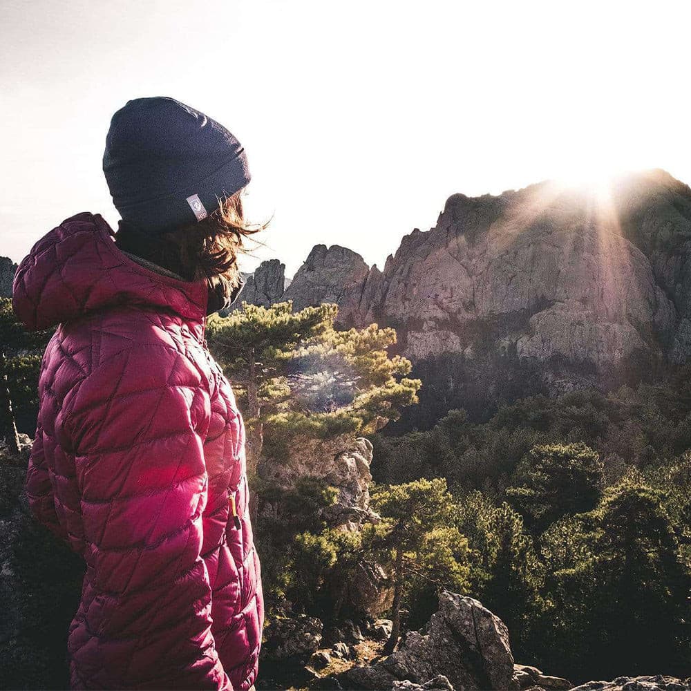 m2 steht auf einem Felsen, blickt auf Sonnenuntergang über bewaldetem Berg.