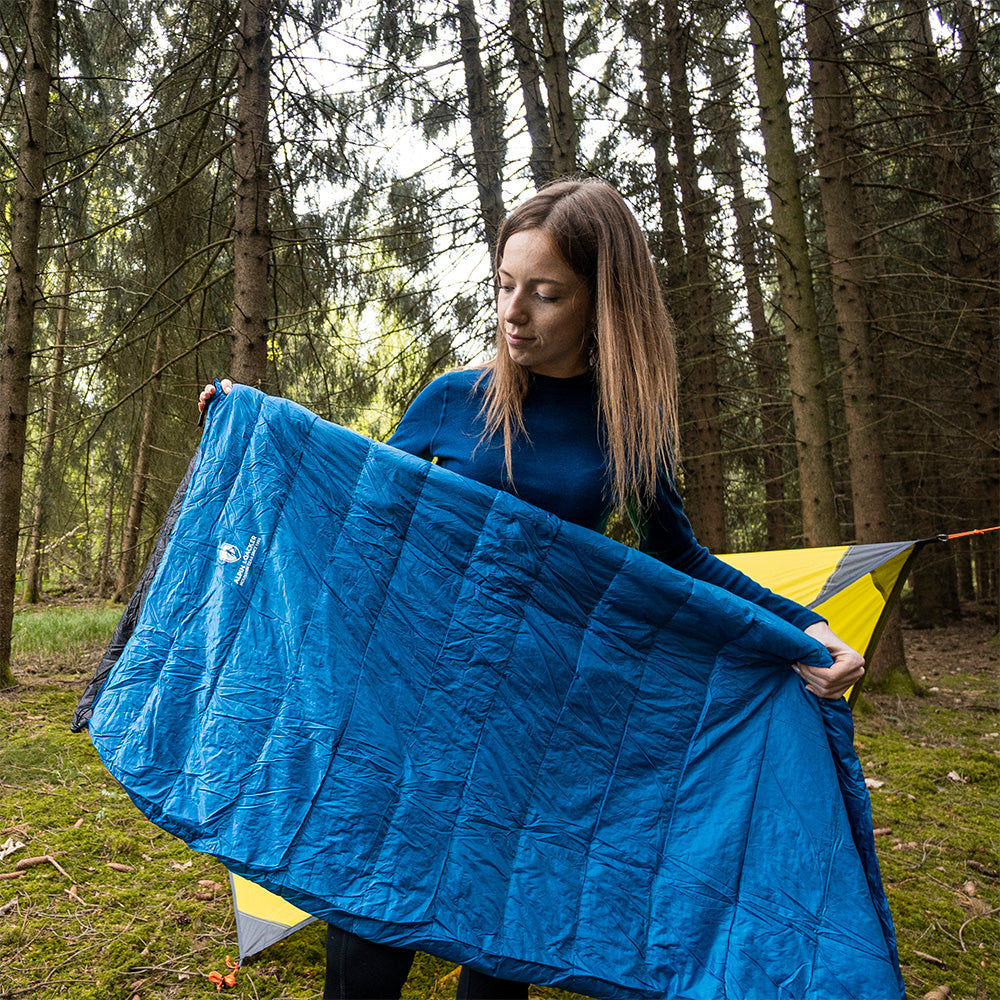 Frau im Wald hält den Leichter Sommer Daunenschlafsack von Alpin Loacker, ideal für Outdoor-Abenteuer, kompakt und ultraleicht.