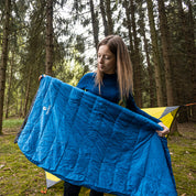 Frau im Wald hält den Leichter Sommer Daunenschlafsack von Alpin Loacker, ideal für Outdoor-Abenteuer, kompakt und ultraleicht.