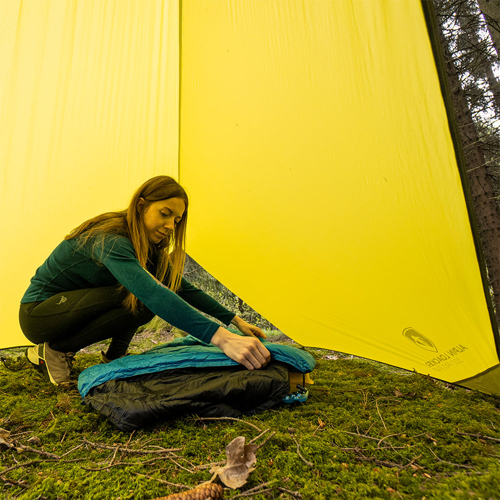Frau bindet den Leichter Sommer Daunenschlafsack zusammen, ideal für Outdoor-Abenteuer, kompaktes Packmaß, perfekt für Trekking und Sommerreisen.