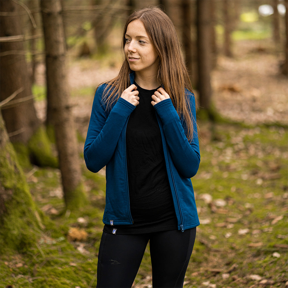 Frau im Wald trägt Merino Jacke Damen 270 g/m², ideal für Outdoor-Abenteuer, mit Wärme- und Feuchtigkeitsregulierung, hoher Bewegungsfreiheit und Komfort.