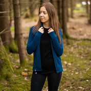 Frau im Wald trägt Merino Jacke Damen 270 g/m², ideal für Outdoor-Abenteuer, mit Wärme- und Feuchtigkeitsregulierung, hoher Bewegungsfreiheit und Komfort.