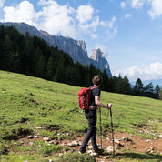 Mann wandert mit Teleskop Wanderstöcken aus Aluminium von Alpin Loacker auf einem grasbewachsenen Hügel, ausgestattet mit Rucksack und Trekkingausrüstung.