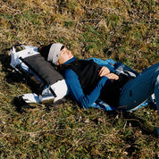 Merino Weste Damen 270g/m2: Person liegt auf Gras, trägt sportliche Wollweste mit Reißverschluss, ideal für Outdoor-Aktivitäten und Freizeit. Perfekter Midlayer für kühle Tage.