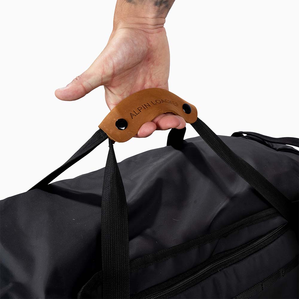 Hand hält Reisetasche, Sporttasche & Duffel Bag von Alpin Loacker, ideal für Reisen und Abenteuer. Rucksackfunktion, wasserabweisend, mit geräumigem Hauptfach und Ledergriff.