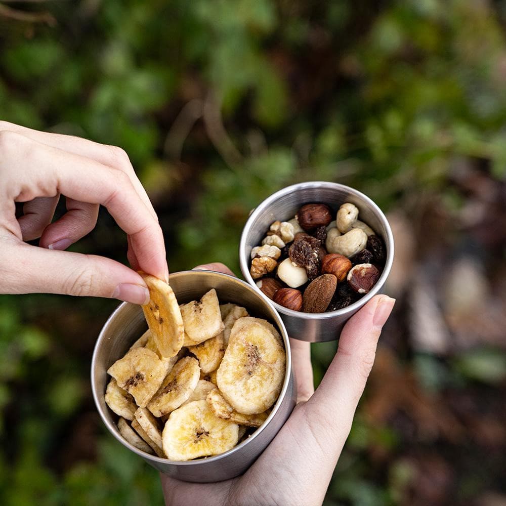 Person hält Schale mit Nüssen und Bananenchips, symbolisch für Alpin Loacker Edelstahl Behälter, ideal für Snacks und Outdoor-Abenteuer.