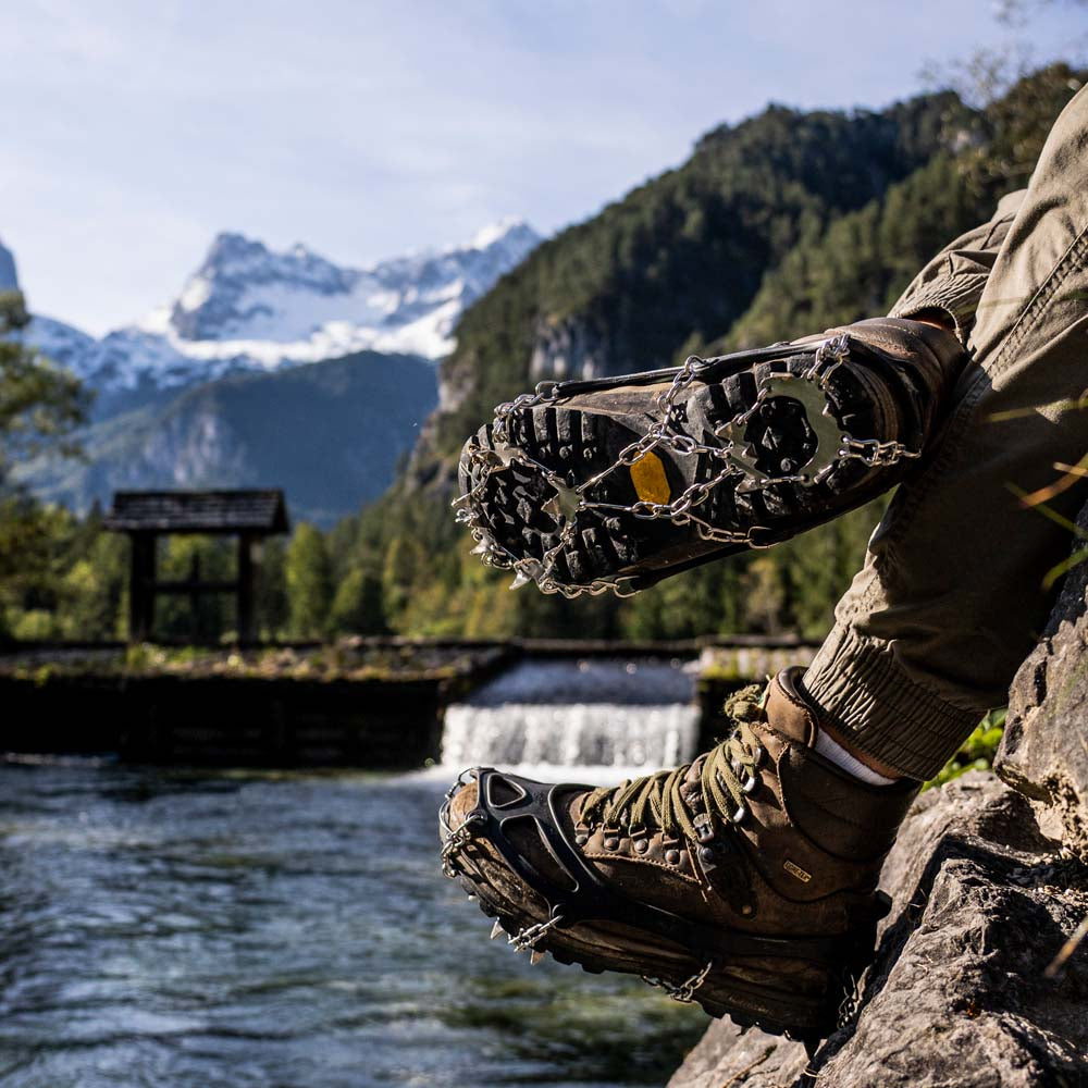 Person trägt Chain Pro 18 Grödel mit Spikes und Schneeketten auf einem verschneiten Weg, ideal für Winterwanderungen und Trekking. Perfekte Stabilität und Haltbarkeit.